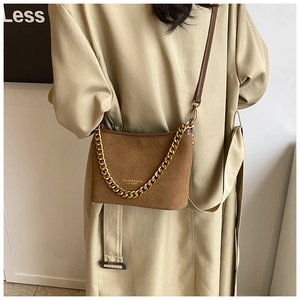 Detail of a brown suede bucket bag featuring a gold chain strap and fashion logo