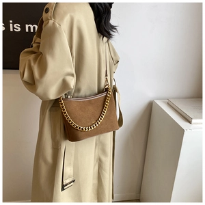 Close-up of brown suede bucket bag featuring a decorative chunky gold chain on a trench coat