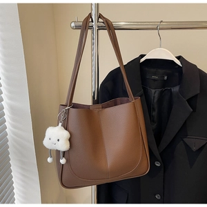 Detail view of large brown leather tote bag with a cute white plush cloud charm accessory