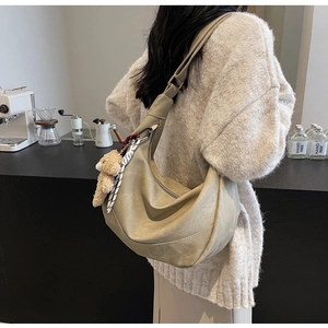 Beigefarbene Hobo-Tasche mit Bärenanhänger in stilvollem Café-Ambiente präsentiert