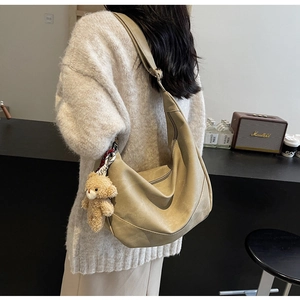 Detail der khakifarbene Hobo-Tasche mit verstellbarem Gurt und süßem Bärenanhänger