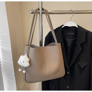 Detail of taupe litchi grain leather tote bag with white cloud plush charm on a hanger
