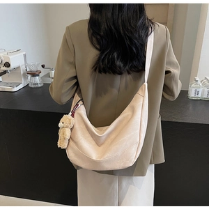 Detail der beige Halbmond-Tasche mit Bärenanhänger, an der Schulter getragen