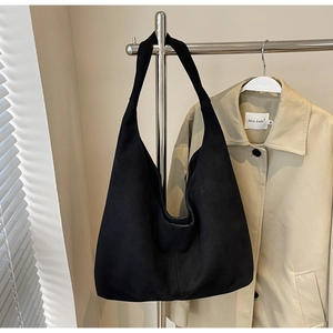 Détail d'un grand sac cabas en daim noir suspendu à côté d'une veste décontractée