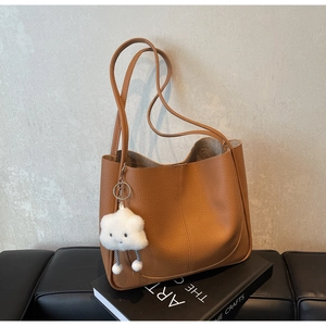 Close-up of brown bucket bag with lychee texture and cute cloud pendant on black sofa
