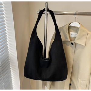 Détail du sac hobo noir en similicuir suédé suspendu à un cintre avec un trench beige