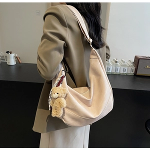 Detailansicht der beigen Halbmond-Tasche mit Plüschbär-Anhänger und kariertem Seidenschal