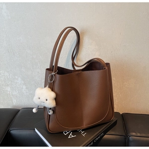Detail of dark brown pebble leather shoulder bag with plush cloud charm and book prop