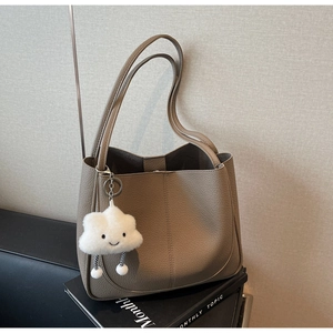 Close-up of khaki lychee texture shoulder bag with white plush cloud charm on books