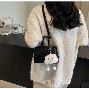Close-up of a black leather crossbody bag with a cute white plush cloud charm on a sweater