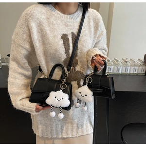Detail of black matte leather handbag with white plush cloud charm and detachable strap