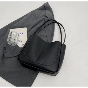 Detail of minimalist black pebbled leather tote bag on grey blazer for daily commute