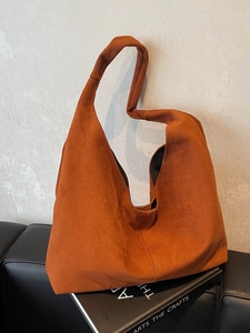 Minimalist burnt orange suede tote bag with stylish knotted strap on a leather chair