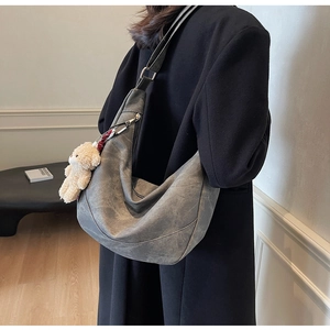 Detail der grauen Hobo-Tasche mit Halbmondform und Plüschbär-Anhänger mit breitem Gurt