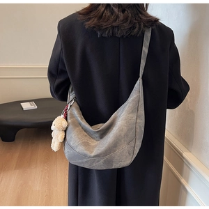 Detailansicht der grauen Halbmond-Tasche mit einem süßen weißen Plüschbär-Anhänger als Zubehör