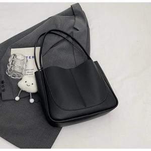 Detail of black lychee grain leather shoulder bag with fine vertical stitching on white bedding