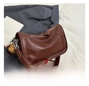 Detail of a brown polished leather half-moon shoulder bag with silver zipper and small charm