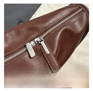 Close-up of brown leather bag featuring silver dual zippers and fine stitching details