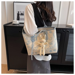 Dettaglio della borsa tote bianco sporco con graffiti blu e ciondolo a coniglio in maglia