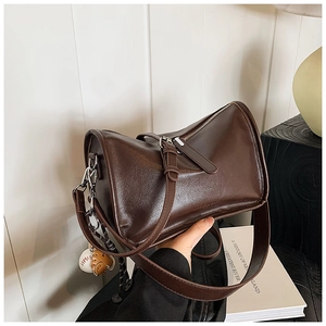 Detail of dark coffee Boston bag with oil-wax texture PU leather and baseball pendant