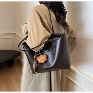 Detail der dunkelbraunen Leder-Shopper-Tasche mit Bärenanhänger und Metalllogo