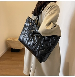 Détail d'un sac cabas noir matelassé porté à l'épaule dans un intérieur au style épuré