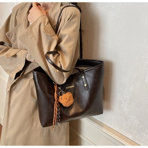 Detail einer dunkelbraunen Tragetasche mit Bärenanhänger und Seidenschal am Trenchcoat