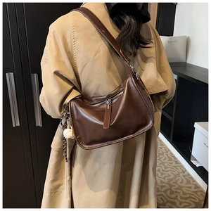 Close-up of brown oiled leather pillow bag featuring a sporty baseball charm accessory