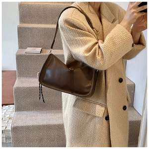 Close-up of vintage brown leather handbag with YA & BAG logo on beige coat outfit