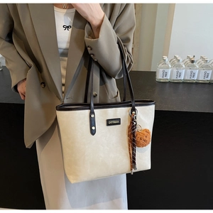 Detail der beigen Shopper-Tasche mit braunen Griffen und Teddybär-Anhänger