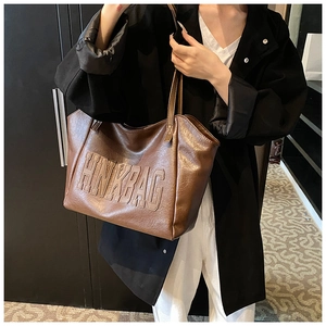 Dettaglio della scritta HNKBAG a rilievo su una grande borsa tote marrone lucida