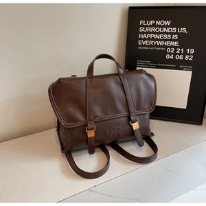 Dettaglio dello zaino vintage in pelle marrone con fibbie dorate e logo a rilievo