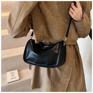 Detail of a black leather crossbody bag with silver zipper and D-ring on urban background