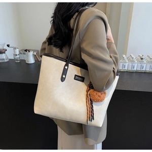 Detailaufnahme der cremefarbenen PU-Leder-Tote mit braunem Rand und Plüsch-Anhänger