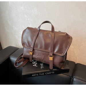 Dettaglio di zaino vintage in pelle marrone con fibbie dorate su divano nero