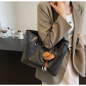 Detail der schwarzen Ledertasche mit Silbernieten und braunem Plüsch-Herzanhänger