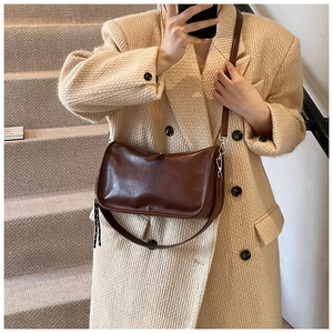 Detail of dark brown leather crossbody bag styled with a beige coat on a staircase
