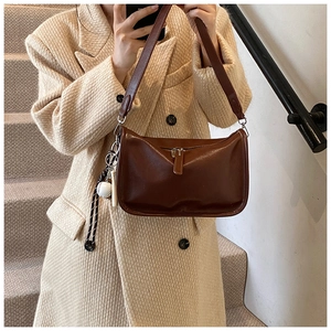 Detail of dark brown leather crossbody bag with vintage sports charm and wide shoulder strap