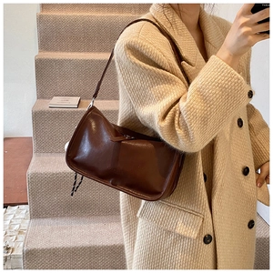 Brown leather baguette bag with silver hardware worn on a beige tweed coat
