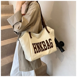 Vista dettagliata della borsa tote in pelle beige con logo HNKBAG portata a spalla
