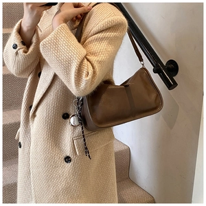 Detail of vintage brown leather handbag with baseball charm worn over a tweed coat