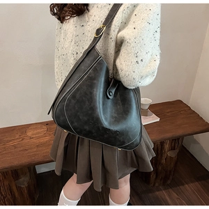 Close-up of black retro bucket bag with white contrast stitching and gold buckle