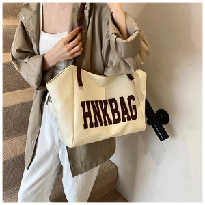 Borsa tote oversize bianco sporco con tracolla marrone portata a spalla da donna