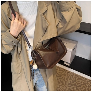 Detail of dark brown leather crossbody bag with baseball charm and sleek zipper closure