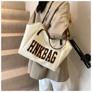 Dettaglio di una grande borsa tote beige con manici marroni indossata da una modella