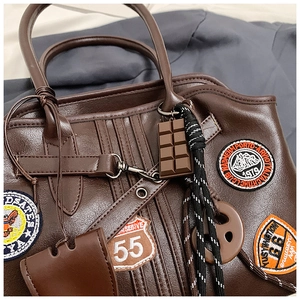 Detailansicht der braunen Retro-Handtasche mit bestickten Badges und Schokoladen-Anhänger