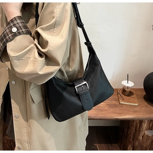 Detail of black pleated crossbody bag with silver buckle worn with a beige trench coat