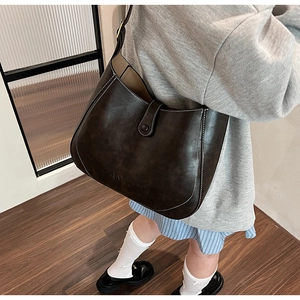 Detail of dark brown leather bucket bag featuring white contrast stitching and logo