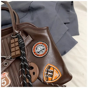 Detail einer dunkelbraunen Ledertasche mit Vintage-Patches und Schokoladen-Anhänger