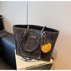 Detailansicht einer großen schwarzen Tragetasche mit Gold-Logo und Bären-Taschenanhänger